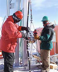 Two AMANDA investigators fasten a light detector to a cable, so the detector can be lowered into the hole melted in the Antarctic ice