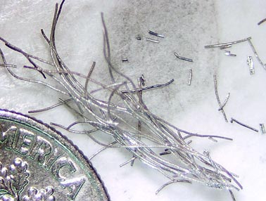 Magnesium diboride wires as they appear after removal from the tantalum tube and part of a U.S. dime for scale.