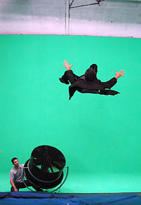 Attached to wires and blown by a wind machine, Brian Greene “flies” through the air against a green screen background, which will be replaced in the editing process by footage of a city street scene. (Photo by Andrea Cross for WGBH)