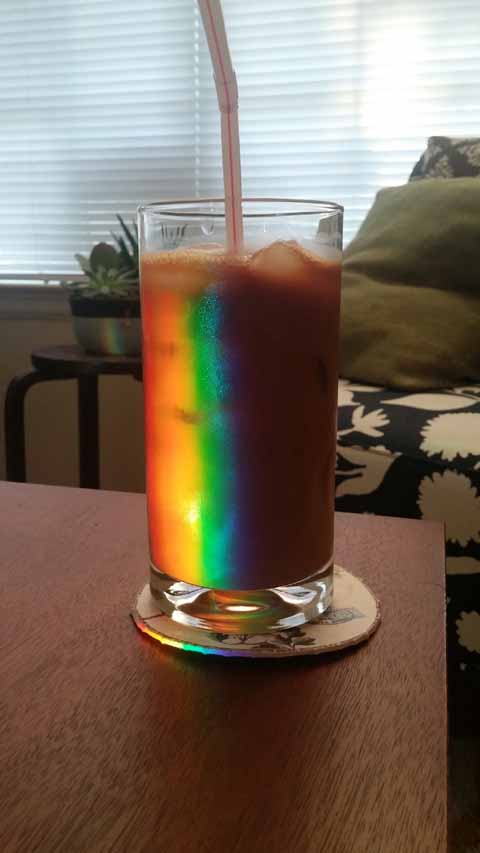 Light bounces off a mirror and refracts through an empty glass to produce a rainbow of color