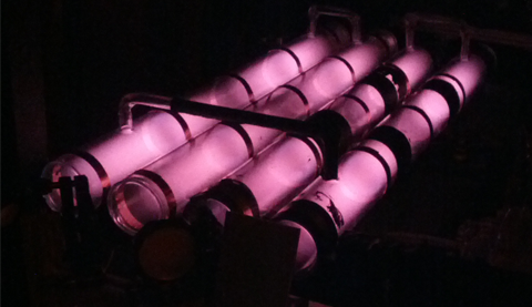 Long tubes of helium glow a soft pink, excited by the radio frequency discharge of the coils wrapped around them.