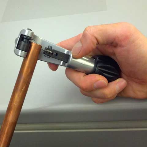 A hand uses a pipe cutter to segment a piece of copper pipe into rings.